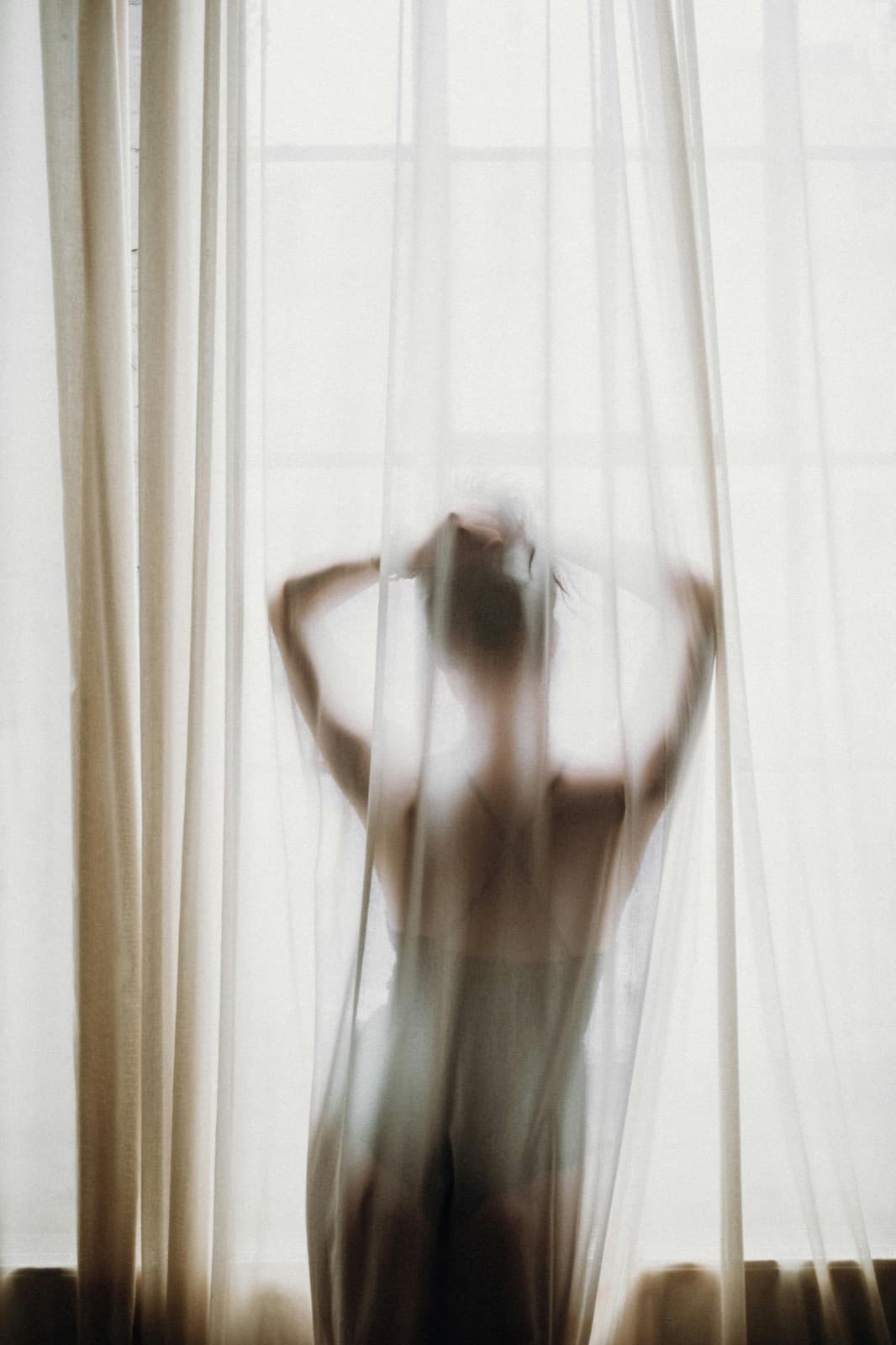 Une silhouette de femme derrière un voilage baigné de lumière